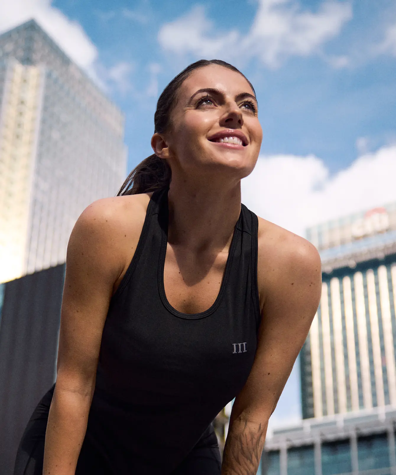 Woman in sportswear smiling after exercise at Canary Wharf, London, with modern skyscrapers in the background, representing health, confidence, and ambition in the Canary Wharf “Where Ambition Lives” campaign.